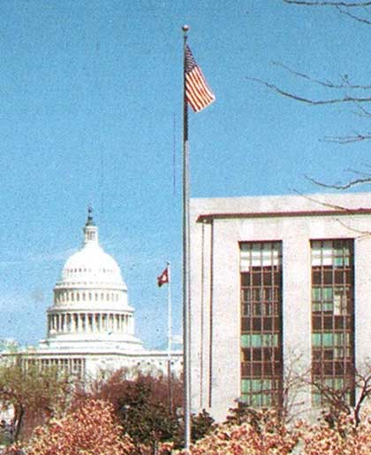 Archive photo of the U.S. Capitol building next to VOA’s headquarters at the Cohen building, with a flagpole vertically dividing the composition.