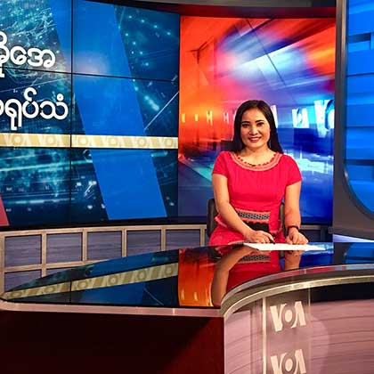 Photo of VOA journalist sitting behind a table in a TV broadcast studio.