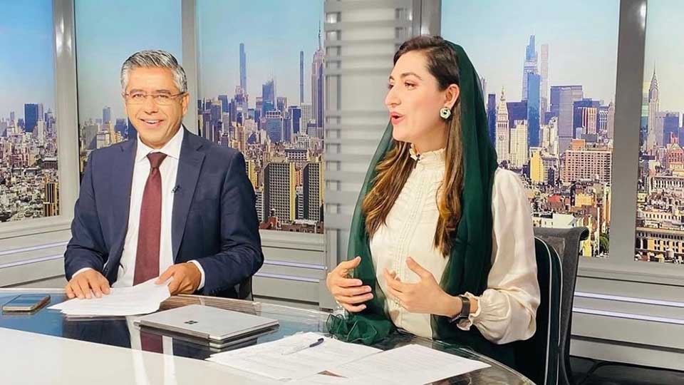 Two VOA journalists reporting from inside a television studio with the New York City skyline in the background.