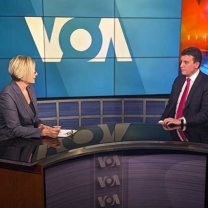 Photo of a VOA journalist interviewing a man at a table in television studio.